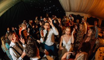 Crowd of guests dancing in a wedding marquee to a dj and sax duo.
