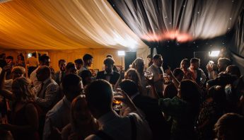 Crowd of guests dancing in a wedding marquee to a dj and sax duo.