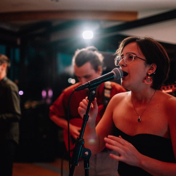 Female vocalist of a Yorkshire wedding band passionately performing with a saxophonist in the background at a wedding reception.