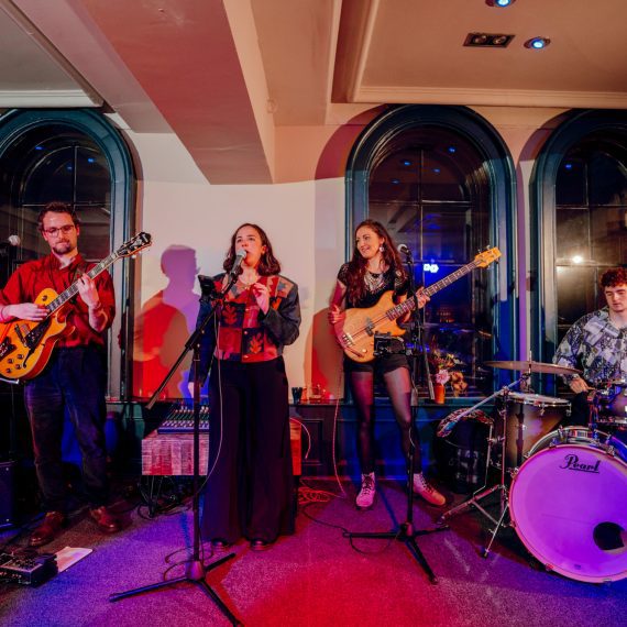 The Cat and Mac Band, a Yorkshire wedding band for hire, engaging with a crowd during a wedding performance, showcasing a guitarist, vocalist, bassist and drummer.